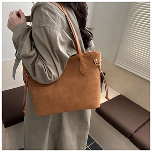 Brown suede tote bag shown on shoulder with drawstring side detail in soft home setting