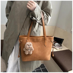 Detail of brown suede tote bag featuring a plush bear charm and side drawstring accents