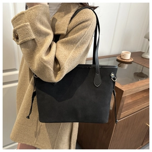 Detail of a black suede tote bag with side drawstring worn with a beige wool coat