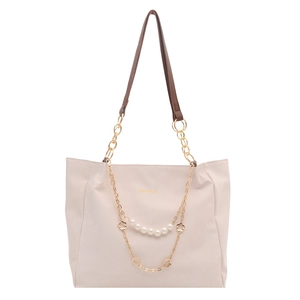 Borsa tote beige chic con catene dorate e ciondoli di perle su uno sfondo bianco