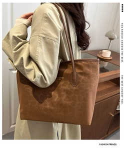 Detail of a large brown suede tote bag with leather strap and gold logo engraving