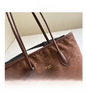 Detailed view of brown suede tote bag with golden branding and cute plush bear charm
