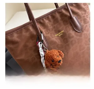 Detail of leopard print tote bag with brown leather handle and cute plush puppy charm