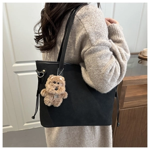 Detail of matte black tote bag with brown plush bear charm and adjustable side drawstring