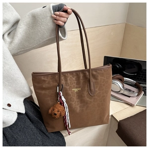 Detail of leopard tote bag featuring gold logo and plush puppy charm with woven rope