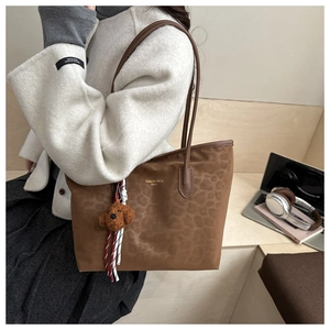 Close-up of leopard print tote bag with brown plush charm and golden brand lettering