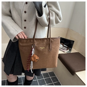 Detailed view of brown tote bag with bear charm and woven straps in office setting