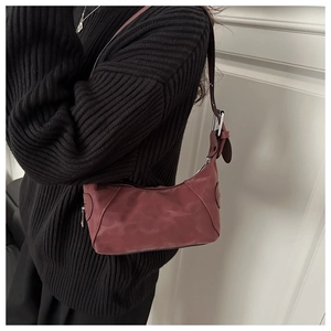 Detail view of a dark red crescent shoulder bag on a model wearing a black knit sweater