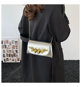 Détail du sac à main argenté métallisé avec boucle ondulée dorée et bandoulière chaîne