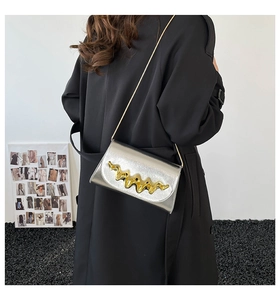 Détail du sac bandoulière argenté brillant avec garniture dorée ondulée et chaîne