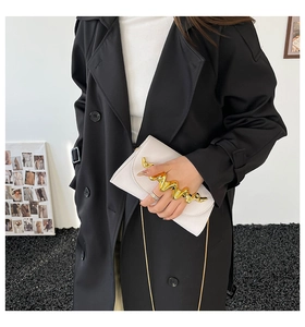 Détail d'un sac à main en cuir blanc avec poignée dorée ondulée et fine chaîne