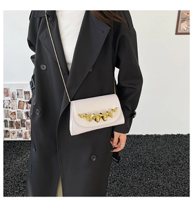 Détail du sac bandoulière crème avec barre métallique dorée ondulée et fine chaîne