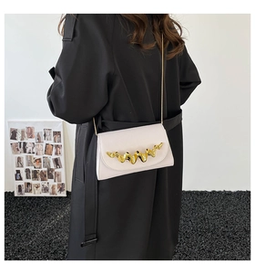 Détail du sac carré en cuir ivoire avec boucle ondulée dorée et bandoulière en chaîne