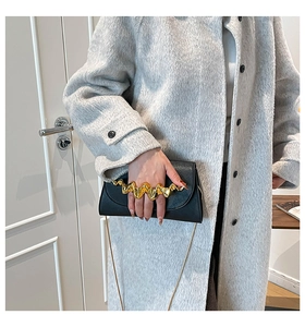 Détail du sac en cuir noir avec poignée dorée ondulée et fine bandoulière en chaîne