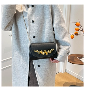 Détail d'un sac bandoulière noir avec boucle dorée ondulée sur un manteau de laine gris