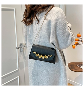 Détail d'un sac de soirée noir à motif ondulé avec chaîne dorée porté par un mannequin