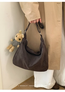 Dettaglio della borsa hobo marrone scuro con ciondolo a orsetto su un trench