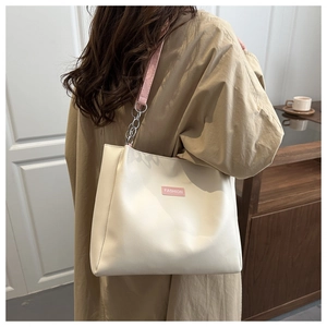 Détail du sac seau crème minimaliste avec étiquette rose et bandoulière en chaîne
