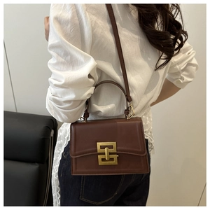 Detail of dark brown retro crossbody bag with gold geometric metal clasp worn by model
