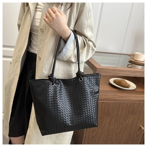 Close-up of black woven leather tote bag with knot strap detail in a lifestyle setting