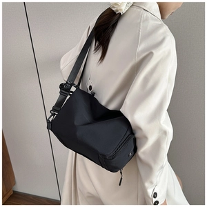 Detalle de un bolso bandolera de nailon negro con correa ajustable sobre una gabardina