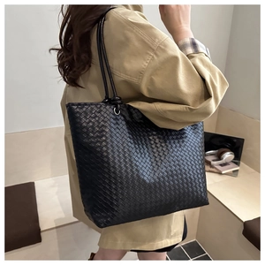 Close-up of a black woven tote bag featuring high-quality leather craftsmanship on model