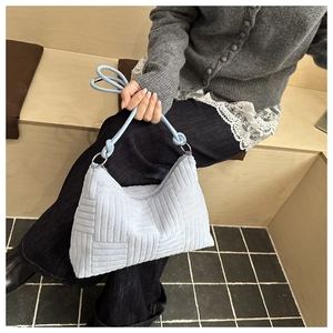 Dettaglio della borsa tote azzurra intrecciata con motivo a maglia tenuta da modella