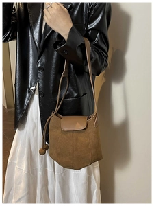 Gros plan d'un sac seau en daim marron avec patchwork en cuir et breloque à pompon