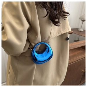 Dettaglio borsa in acrilico blu elettrico metallizzato con catena d'oro su cappotto beige