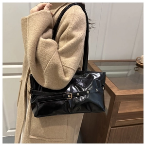 Detail of glossy black shoulder bag featuring gold buckle belt and metallic eyelets