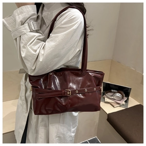 Detail of wine red glossy leather tote bag showing the metal buckle and shoulder straps