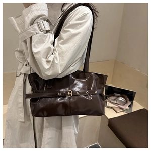 Detail of dark brown glossy tote bag with decorative buckle strap worn with a trench coat