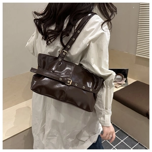 Detail of deep brown patent leather tote bag with gold metal eyelets and buckle accents