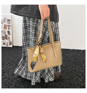 Detail of khaki tote bag featuring metal logo and decorative orange printed silk scarf