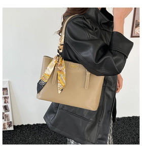 Detail of khaki leather tote bag with yellow silk scarf and fashion logo plate