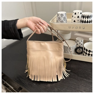 Detail of a beige tassel bucket bag showing its dense fringe texture and PU leather strap