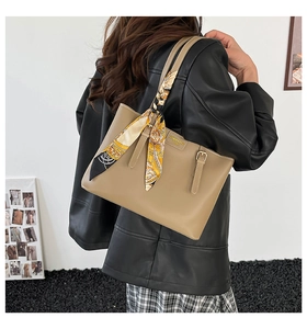 Detail of khaki leather tote bag featuring a bright yellow floral scarf on the strap