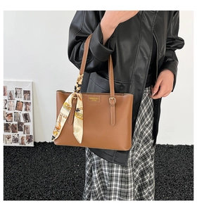 Detail of classic brown tote bag with silk scarf and gold embossed logo on textured leather