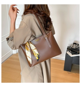 Detail of a brown leather tote bag with a decorative geometric silk scarf on the handle