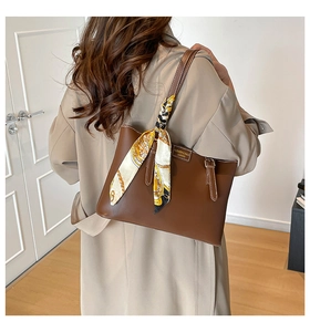Detail of a brown leather tote bag with floral silk scarf on a light trench coat