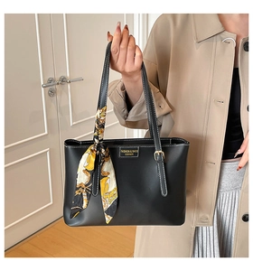 Detail of black leather tote bag with white stitching and decorative silk scarf accessory