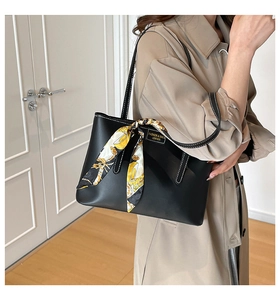 Detail of black leather tote bag featuring a decorative patterned silk scarf on the handle