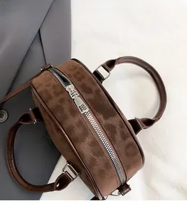Close-up of matte suede texture with silver metal zipper and brown leather handle