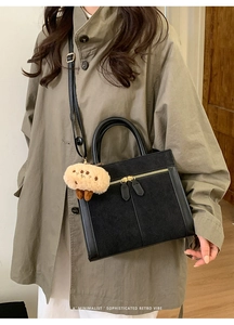 Détail du cabas noir en daim et cuir avec zips dorés et pendentif en peluche doux
