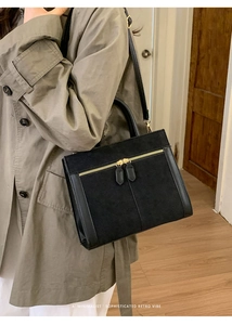 Detail of minimalist black square bag featuring gold dual zippers and mixed textures