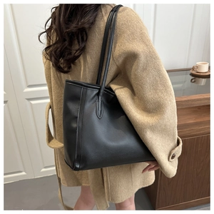 Detailed view of a large black tote bag worn with a camel coat in a minimalist interior