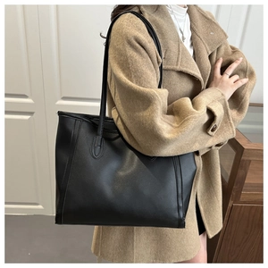 Detail of a large black leather tote bag with vertical stitching on a wool coat