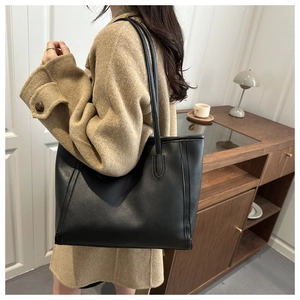 Minimalistische große schwarze Tragetasche zu einem beigen Wollmantel getragen