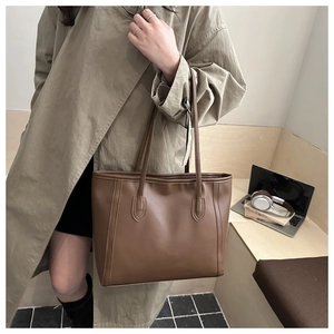 Brown faux leather tote bag shown on shoulder in a minimalist urban commuter setting