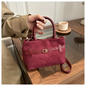 Detail of burgundy faux suede tote bag showing gold buckle and smooth leather handles